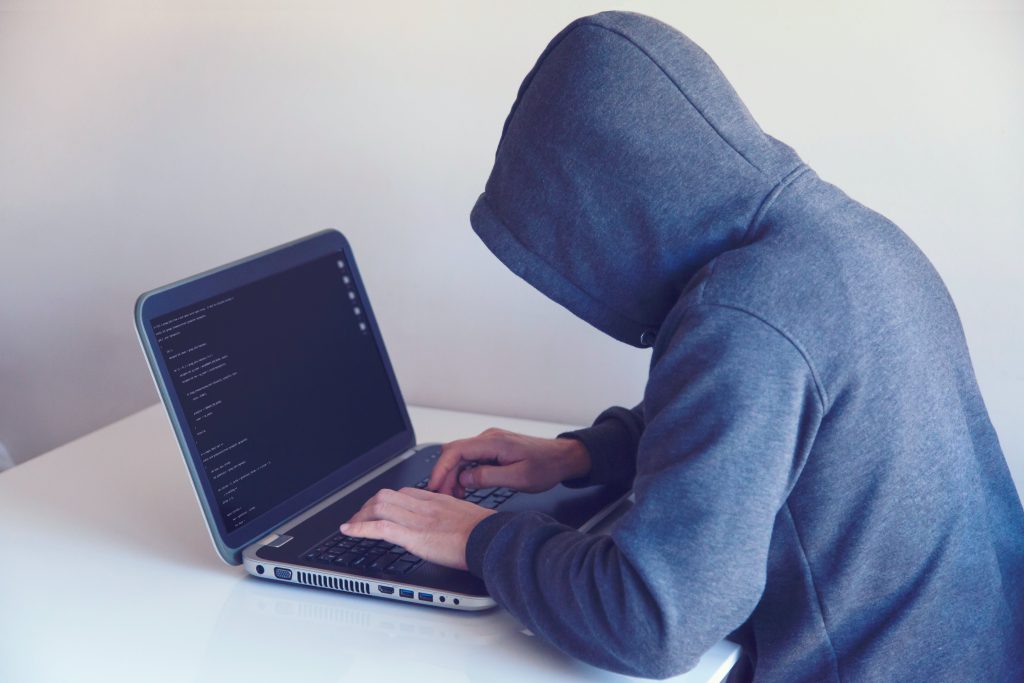 A picture of a hooded figure over a computer screen symbolizing a cyber hacker.